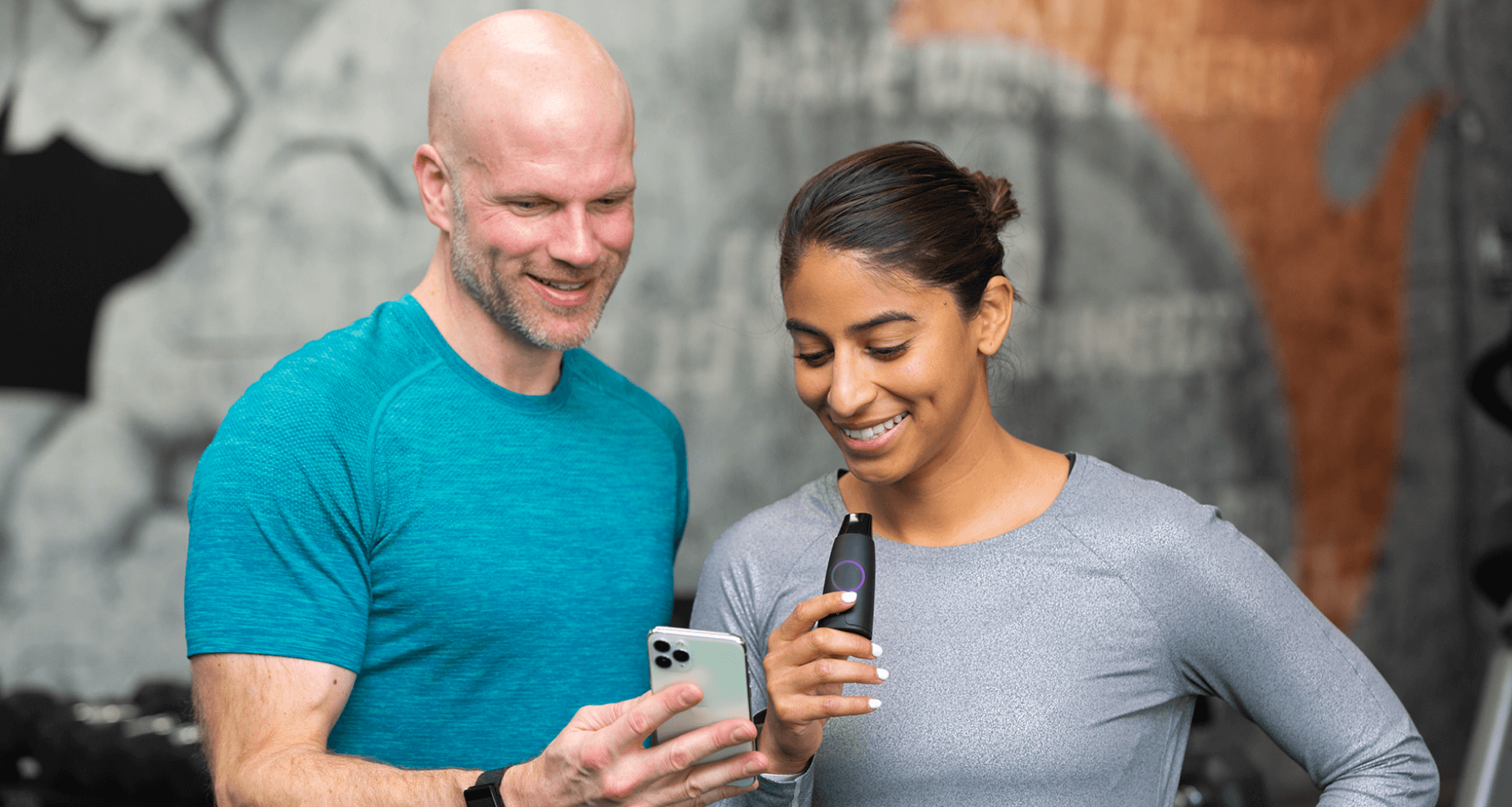 A man and a woman are smiling, the man is holding a cell phone and the woman is holding a Lumen device
